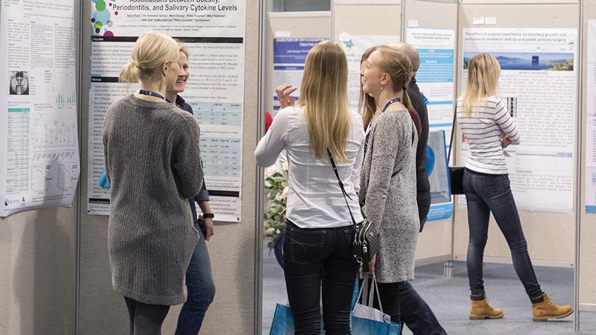 Ihmisiä posterinäyttelyssä keskustelemassa.