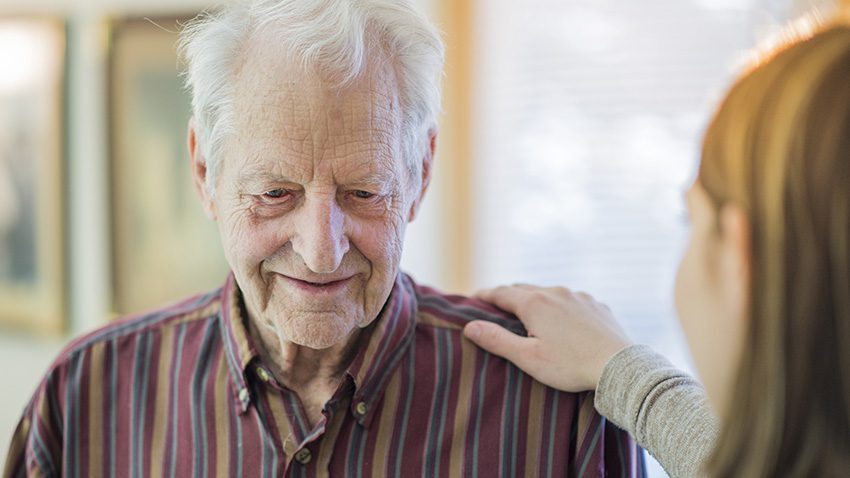 Iäkäs mies ja hoitajan käsi olkapäällä