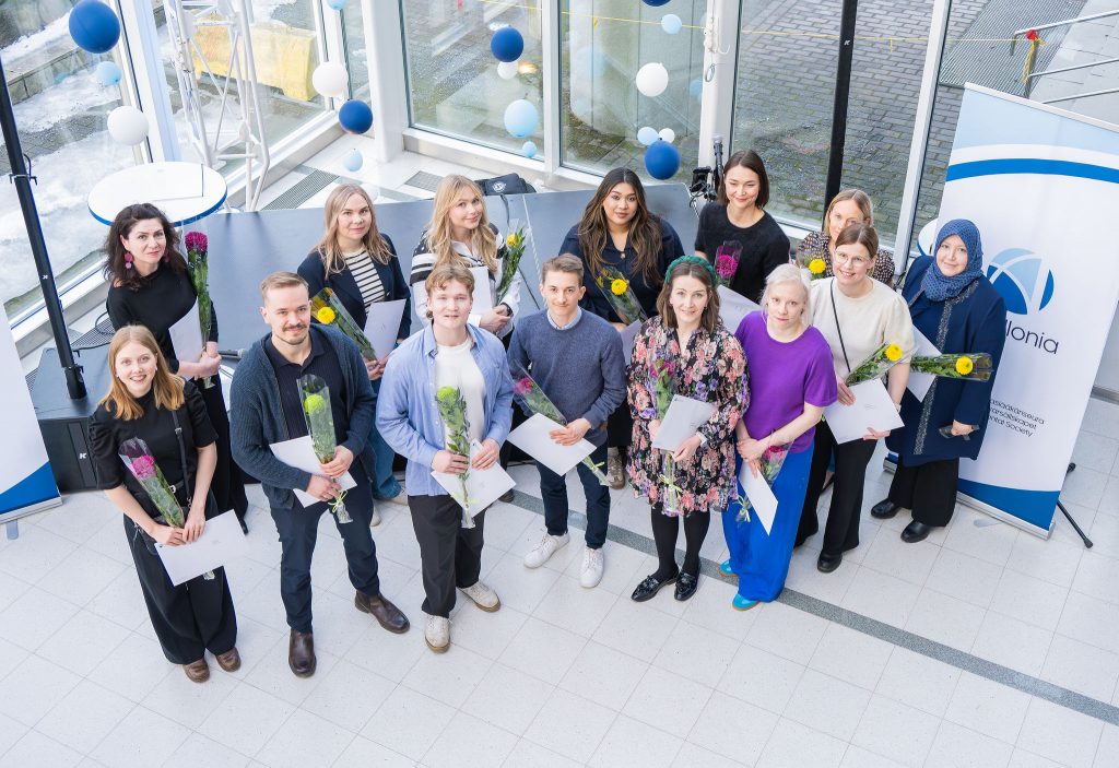 Apurahojen saajia 2026 Kuvassa joukko apurahansaajia kunniakirjojen ja ruusujen kanssa Tampere-talon talvipuutarhassa.